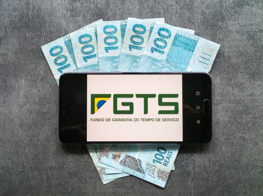 Celular com o aplicativo FGTS sobre cédulas de R$ 100: lucro do Fundo de Garantia distribuído aos trabalhadores